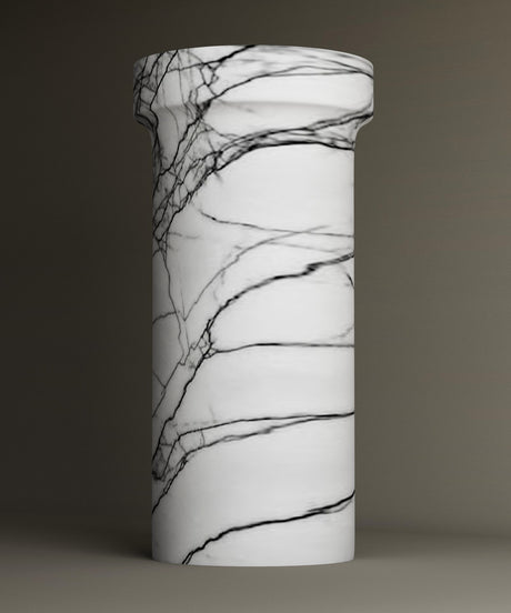 The TRAVERTABLE Lilac Marble Pedestal Vanity Sink features a freestanding cylindrical design with a white base and striking dark veining, shown against a plain, neutral background.