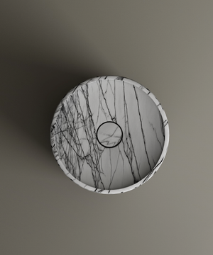 The Lilac Round Marble Pedestal Vanity Sink by TRAVERTABLE, crafted from white natural stone with dark gray veining, is displayed from above on a matte gray surface. The centered drain and sculptural form cast a subtle leftward shadow.