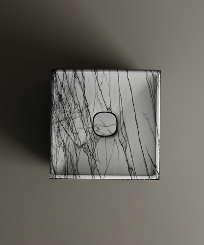 The TRAVERTABLE Lilac Square Marble Pedestal Vanity Sink features a lilac marble pattern with dark gray veins and a centered black button, showcased on a neutral surface for subtle architectural style.