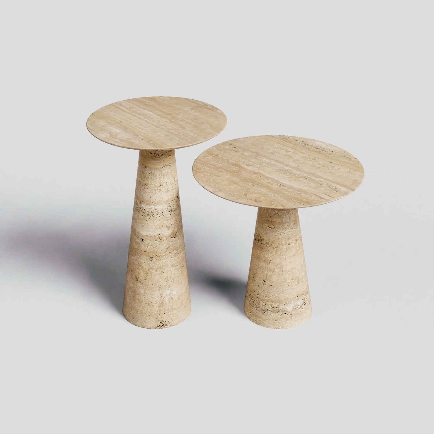 The Twin Pillars Travertine Side Table Set by Travertable features two round, beige stone tables on a light grey background. Their conical bases and textured elegance echo natural travertine artistry, creating harmonious architectural balance.