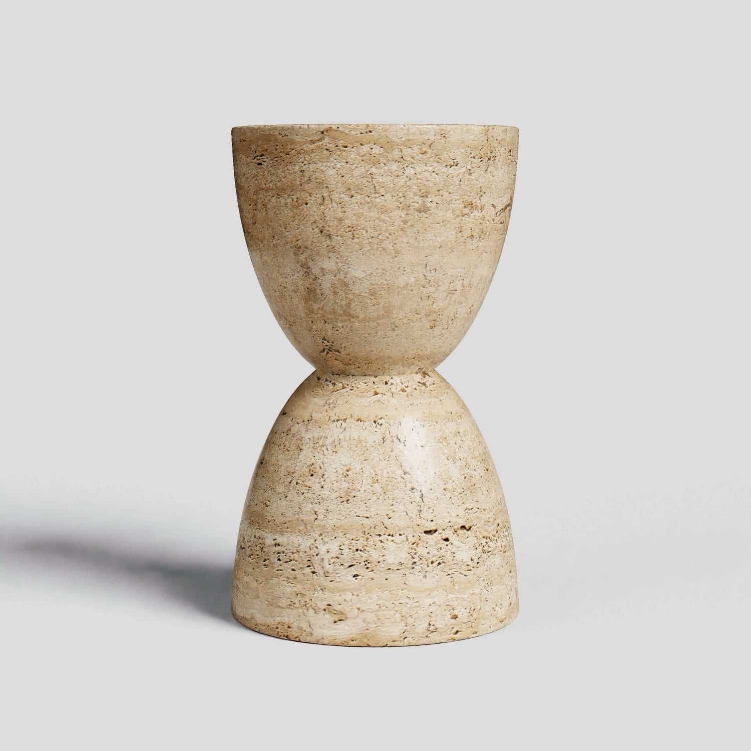 The Eda Beige Travertine Sphere Table by Travertable is a minimalist stone hourglass stool with a smooth, textured beige surface. Its two rounded halves elegantly meet at the center against a light gray background, capturing the essence of travertine table design.