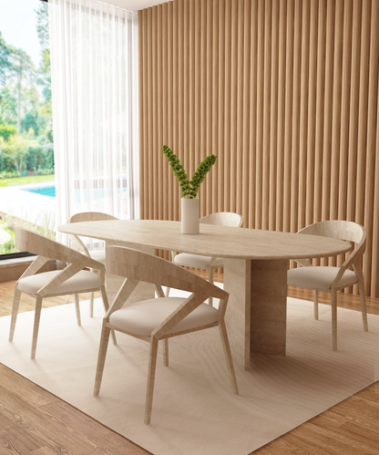 A modern dining room features the TRAVERTABLE Oval Travertine Dining Table with Split-V Pedestal Base, six matching chairs, a white vase with greenery, wood slat wall paneling, a large window, and views of lush green and a pool outside.
